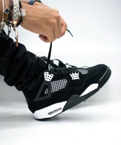Person tying the black and white sneaker laces, with multiple bracelets on their wrist visible.