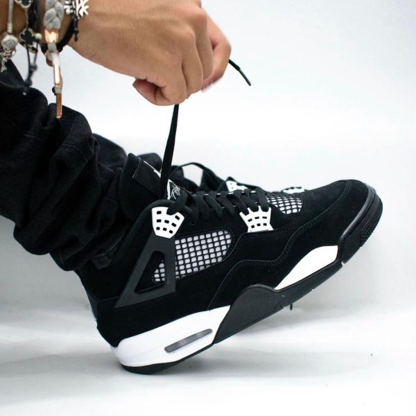 Person tying the black and white sneaker laces, with multiple bracelets on their wrist visible.
