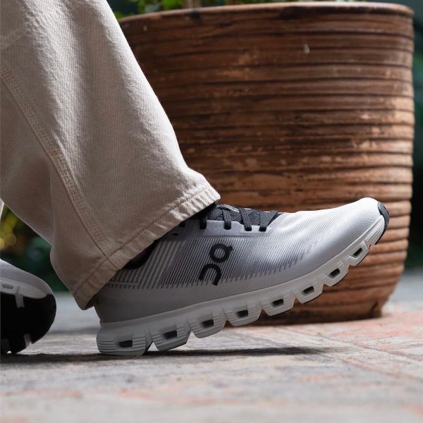 Close-up of a gray running shoe on a person’s foot, beige pants, stepping on a paved surface with a wooden planter in the background.
