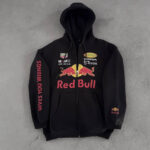 Black zip-up hoodie with Red Bull logos and sponsor names on chest, 'Gives You Wings' text along the left sleeve, laid flat on concrete.