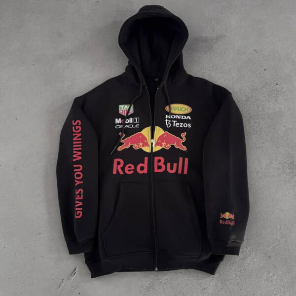 Black zip-up hoodie with Red Bull logos and sponsor names on chest, 'Gives You Wings' text along the left sleeve, laid flat on concrete.