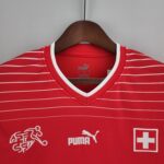 Red striped Puma athletic jersey on a wooden hanger against a gray wall, with Puma branding and a Swiss flag patch visible on the chest area.