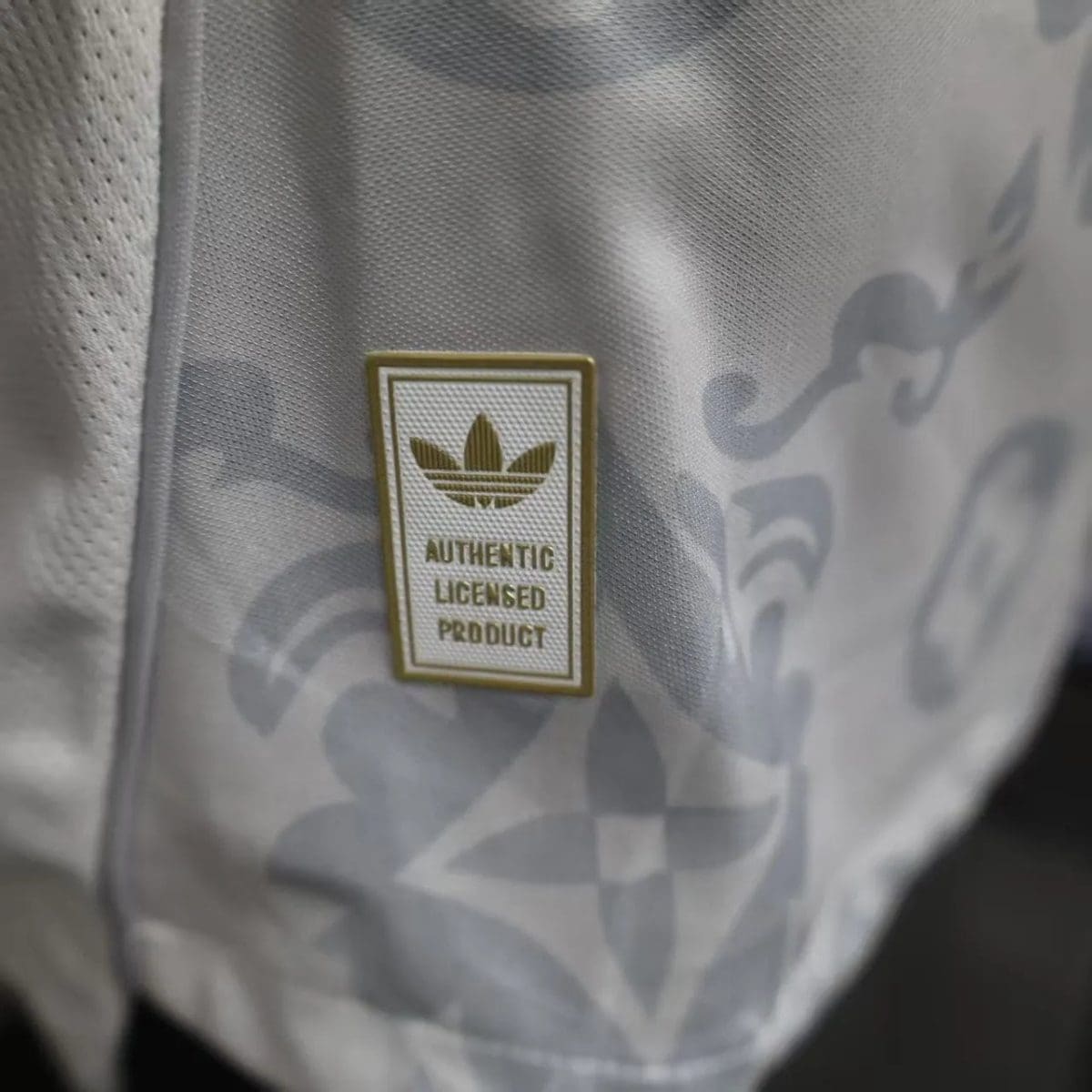 Close-up of gray fabric with a small rectangular badge reading 'AUTHENTIC LICENSED PRODUCT' and a trefoil logo above the text.