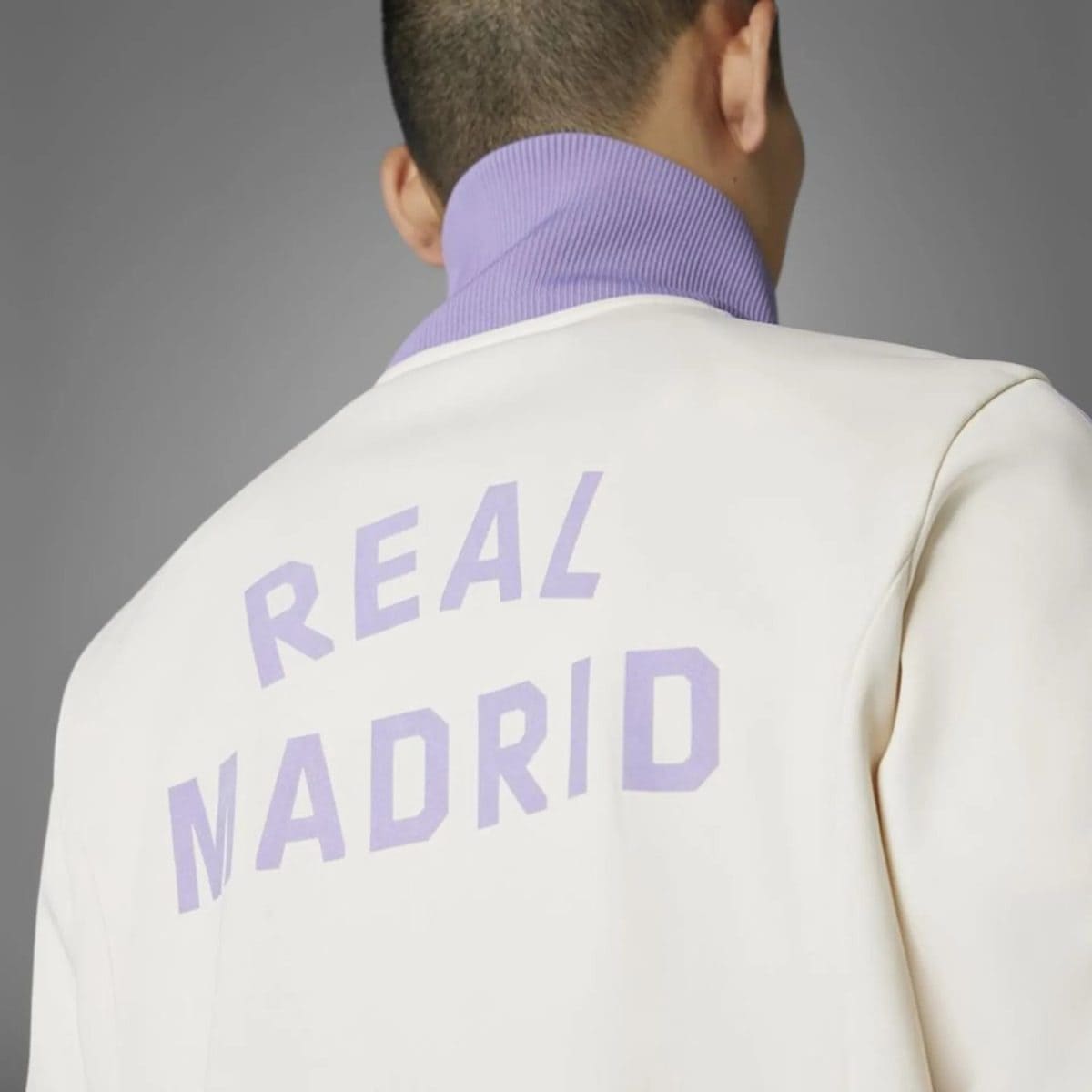 Back of a person in a white jacket with a lavender shirt; large purple 'REAL MADRID' text visible on the back.