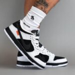 White and black high-top Nike sneakers worn with white crew socks; a tattooed leg is visible in the background.