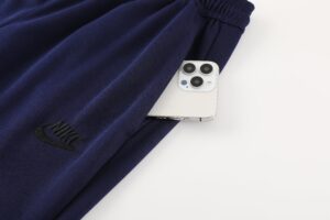 White iPhone with triple camera rests under a dark blue Nike drawstring bag on a white surface, visible near the bag’s edge.