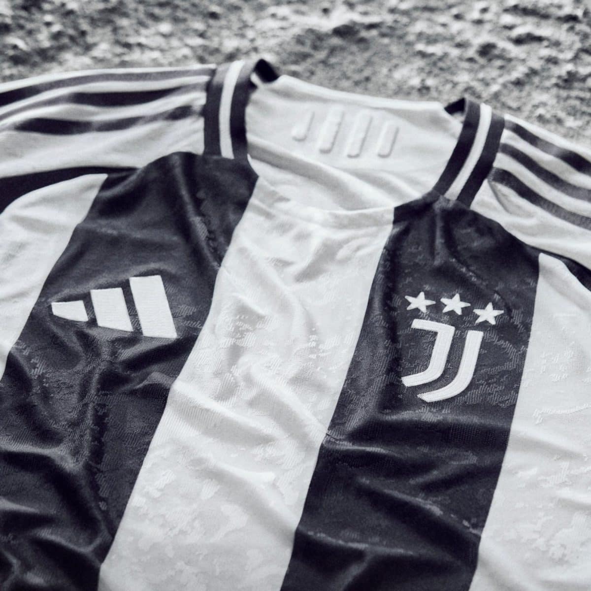 Close-up of a black-and-white Juventus football jersey fabric showing part of the crest and raised stars, with textured material