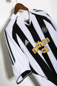 Newcastle United football jersey with black and white vertical stripes, sponsor Northern Rock, hanging on a wooden hanger.