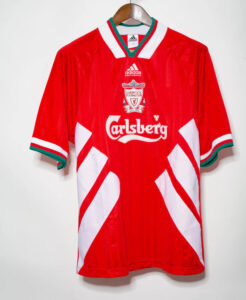 Red Liverpool FC football jersey featuring white diagonal panels, Carlsberg sponsor, and Adidas branding on a hanger.