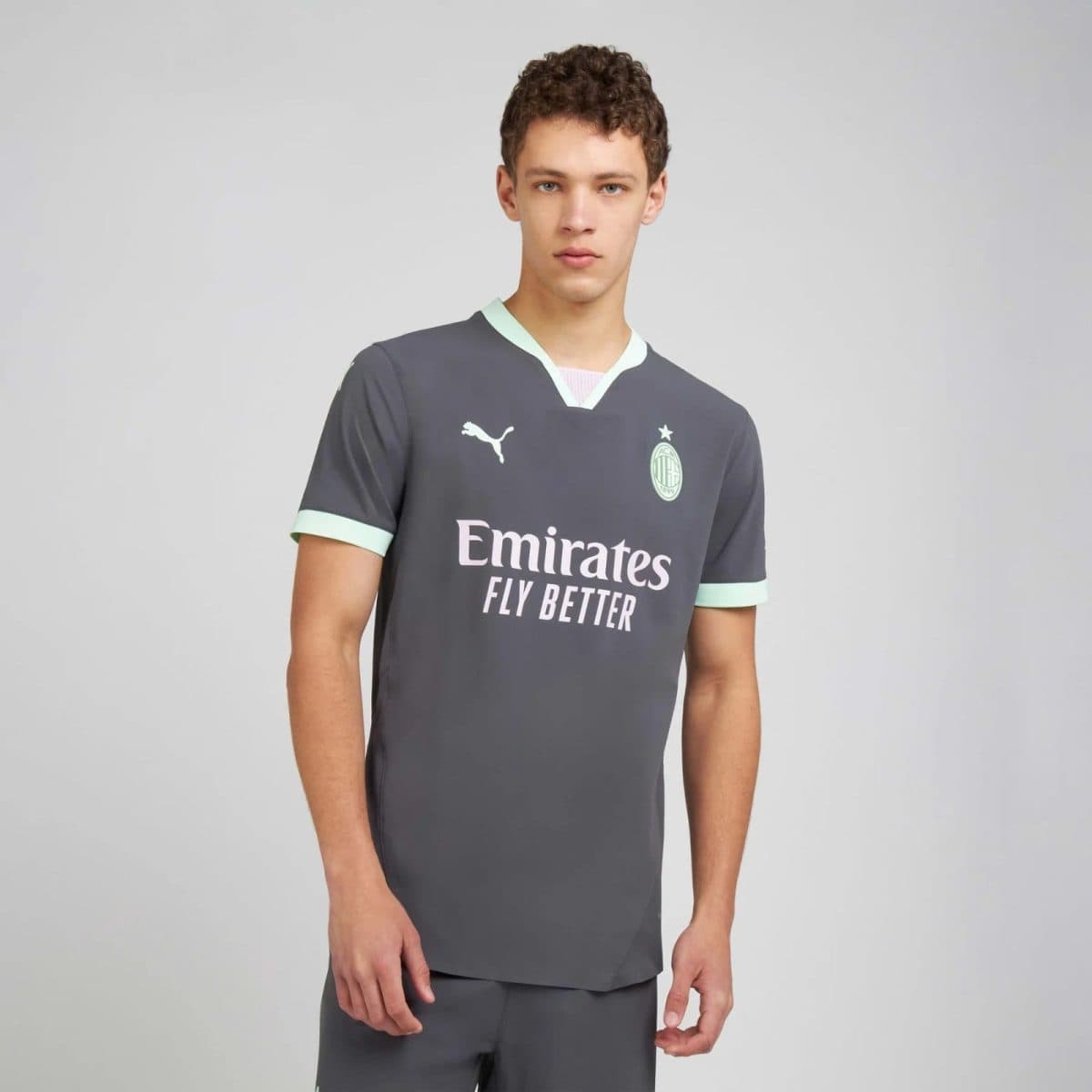 Young man modeling a dark gray football jersey with mint-green trim and a light sponsor logo on the chest, standing against a plain background.
