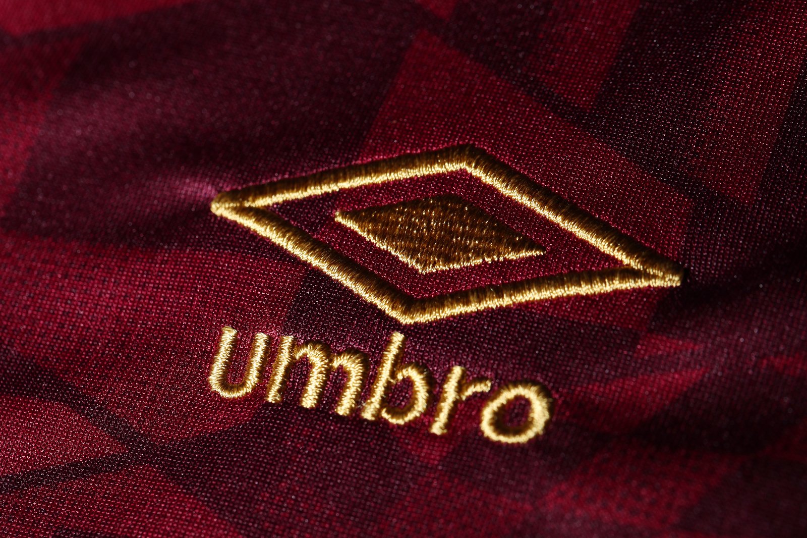 2H5weQAbgJu2SBq | UAE SPORT STORE Close-up of gold embroidered Umbro diamond logo on maroon fabric (jersey).