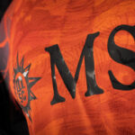 Close-up of an orange jersey with large black letters 'MS' and a star emblem on the left.