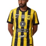 Man wearing a yellow and black striped soccer jersey with logos and crest visible on the chest.