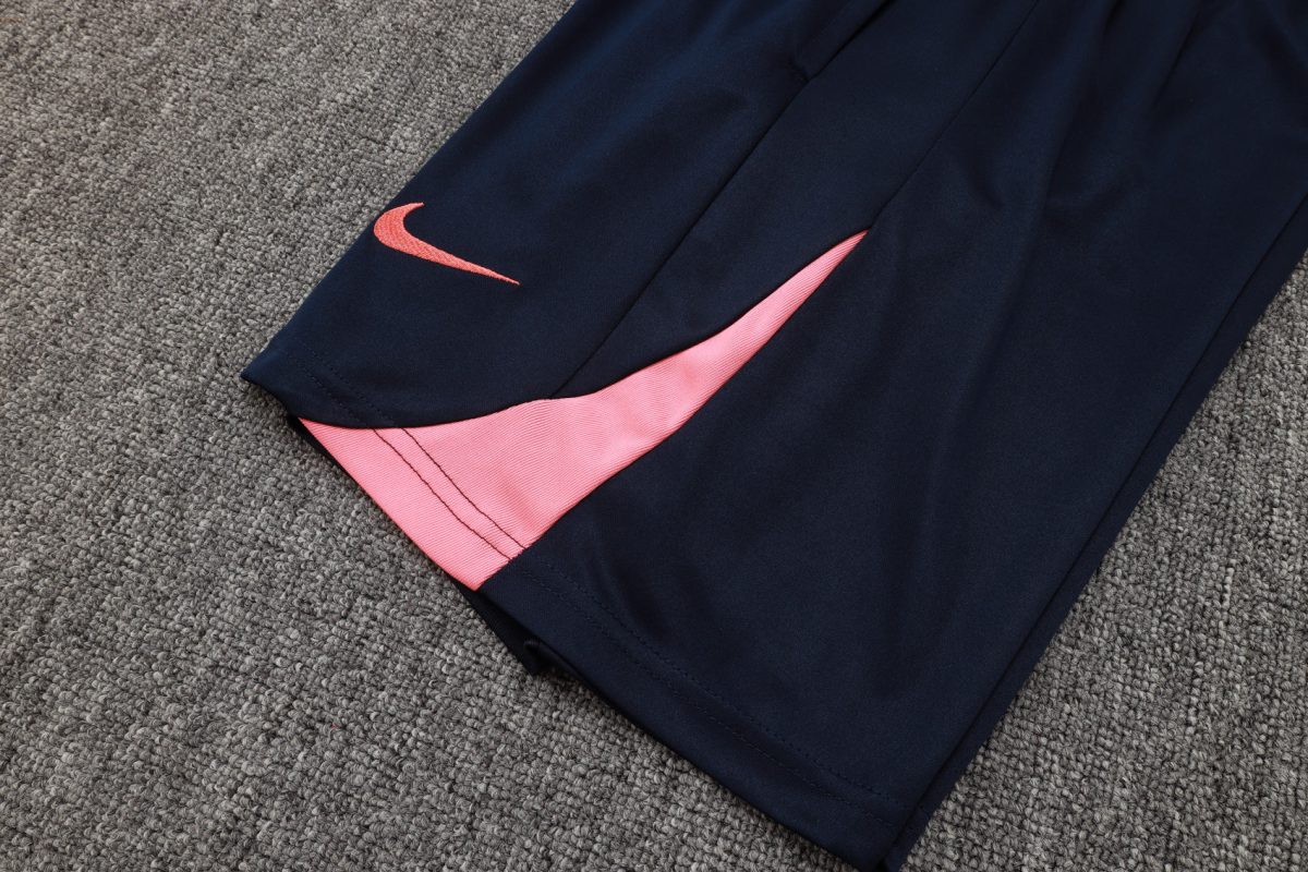 Navy athletic pants with a pink side panel and pink Nike swoosh on the leg, lying on a gray carpet.