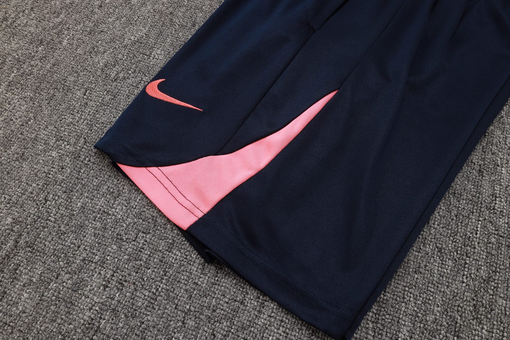 2a00b1bf | UAE SPORT STORE Navy athletic pants with a pink side panel and pink Nike swoosh on the leg, lying on a gray carpet.