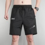 Man wearing black athletic shorts with a drawstring waist; visible Under Armour logo on left thigh and patterned fabric texture.