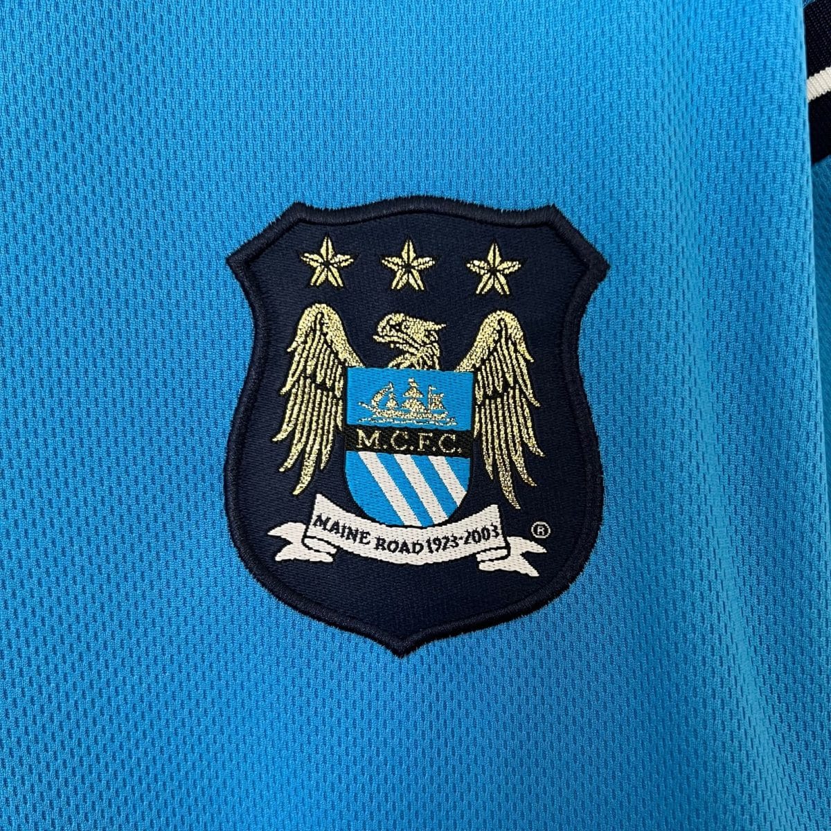 Close-up of blue jersey fabric with an embroidered shield badge and three gold stars at the top.