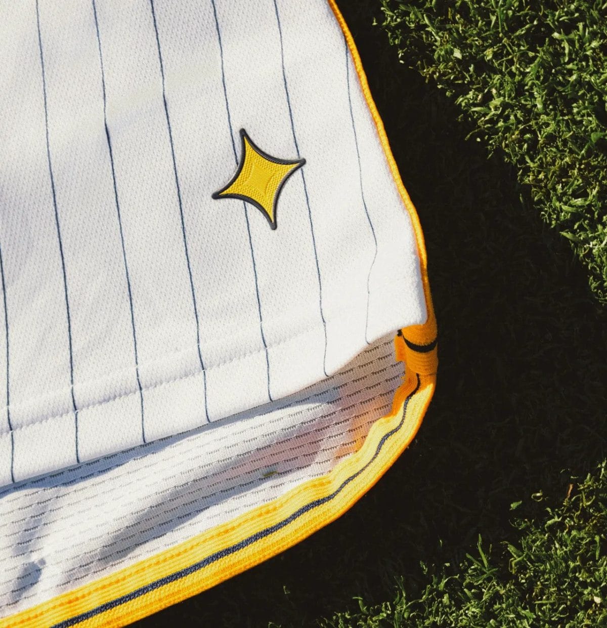 Close-up of white fabric with blue vertical pinstripes and bright yellow edging on green grass.