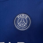 PSG logo patch on blue fabric, circular badge with Eiffel Tower motif and 'PARIS SAINT-GERMAIN' text