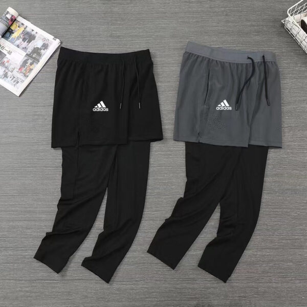 Two pairs of Adidas athletic pants with overlaying shorts (black and gray) laid flat on a wooden floor, logo visible on each pair.