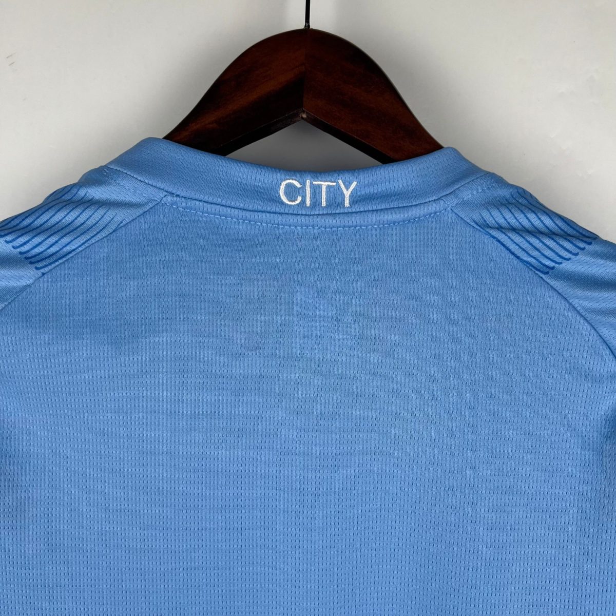 Blue polo shirt on a wooden hanger, shown from behind with the word 'CITY' embroidered on the collar.