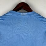Blue polo shirt on a wooden hanger, shown from behind with the word 'CITY' embroidered on the collar.