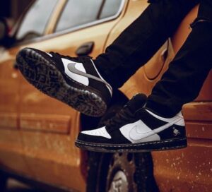 Pair of black-and-white Nike sneakers resting on a yellow/orange car, one foot propped up on the wheel area.