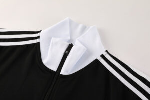 Close-up of a black Adidas track jacket with a white collar, front zipper, and white stripes along the sleeves.