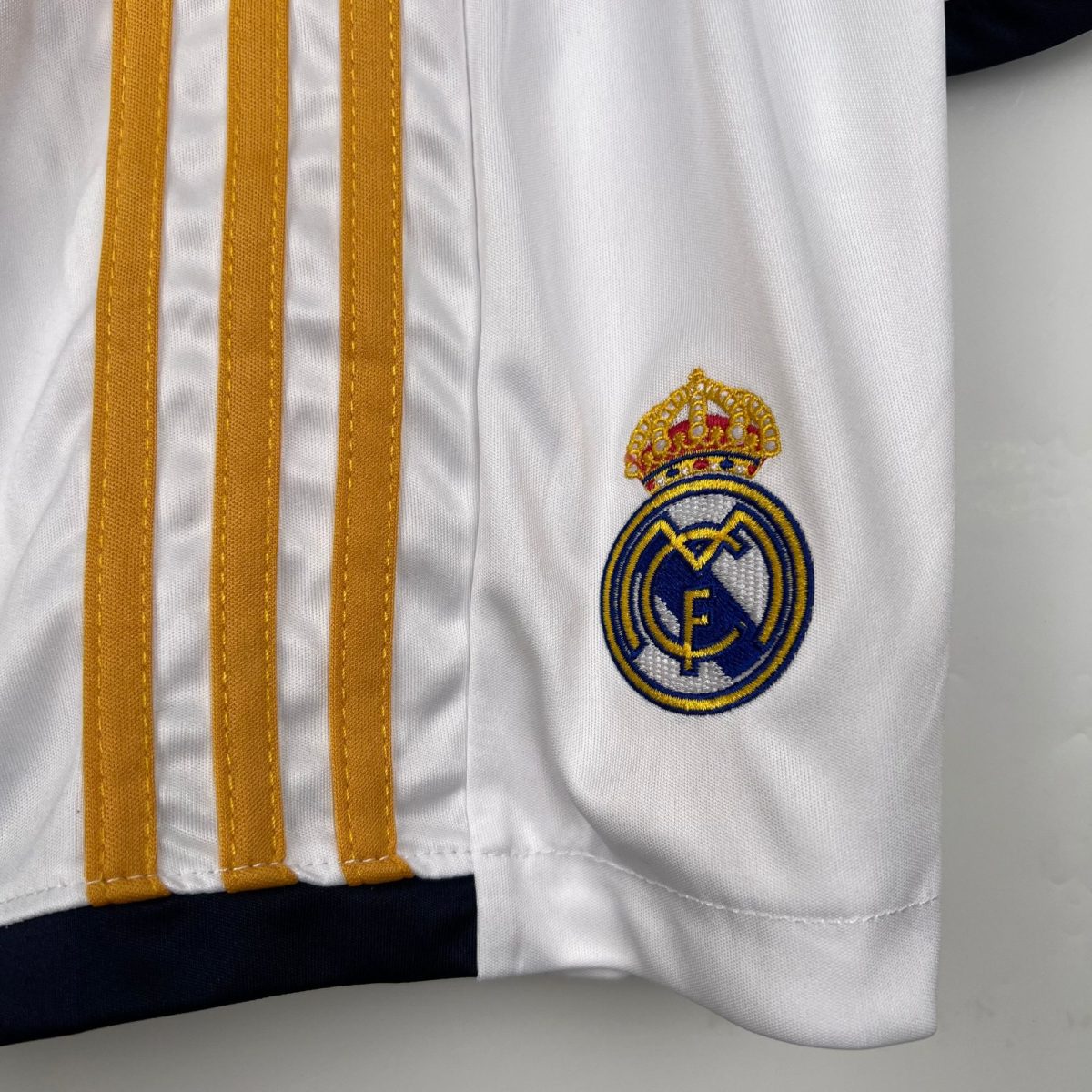 Close-up of a white Real Madrid jersey showing gold vertical stripes and part of the club crest.