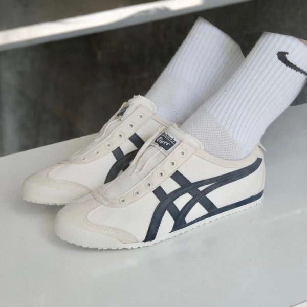 White Onitsuka Tiger sneakers with dark stripes, worn with white crew socks, resting on a pale surface.
