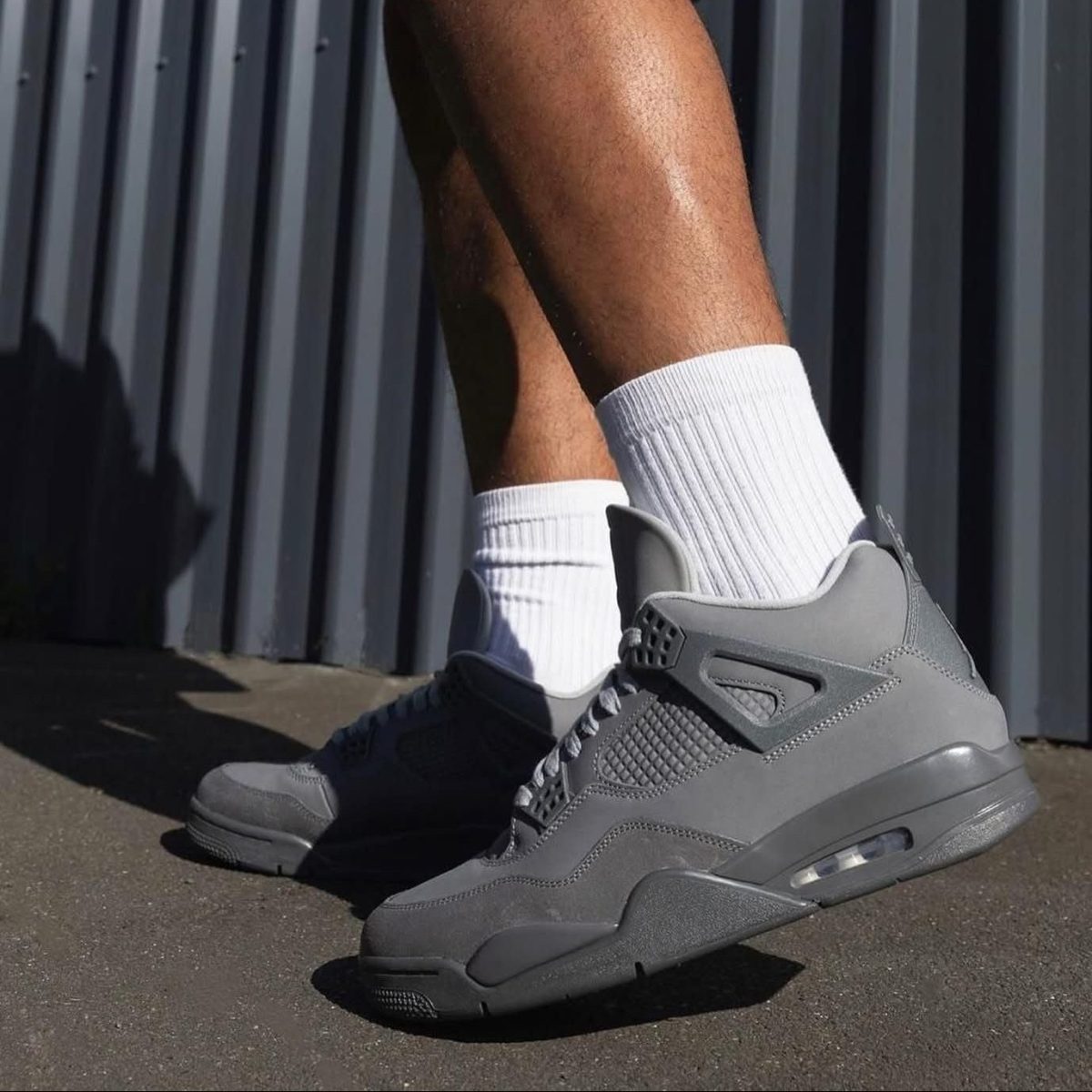 Close-up of a person wearing gray sneakers and white crew socks standing on pavement beside a metal fence/wall.