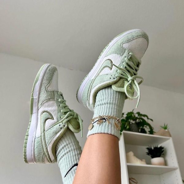 Mint green suede sneakers with white soles and laces, worn with light blue ribbed socks, indoors near a plant-filled shelf.