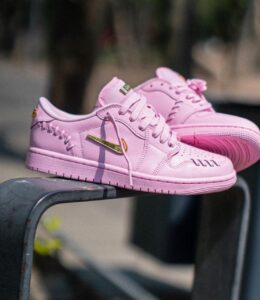 Pair of pink Nike sneakers with a gold swoosh resting on a metal railing outdoors.