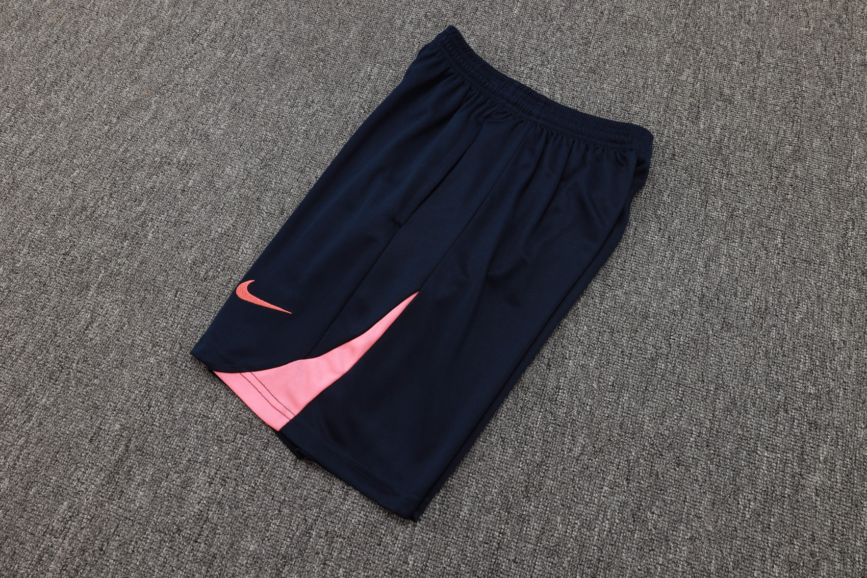 2cd95220 | UAE SPORT STORE Navy athletic shorts with a pink Nike swoosh and pink panel on the leg, laid on a gray carpet.