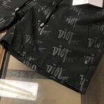 Black fabric with a repeating Dior Paris logo pattern; zippers and hardware visible, suggesting a designer jacket or bag piece.