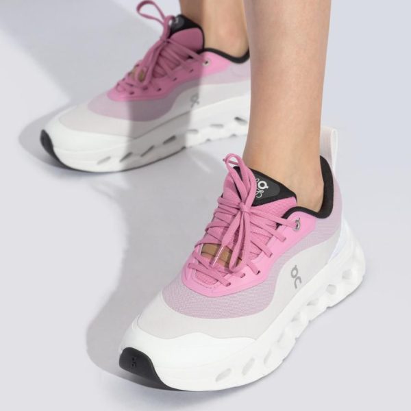 Pink and white athletic sneakers on a person’s feet with a chunky white sole and pink laces against a light gray background, styled for sport or fashion.