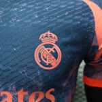 2dadb7c2 | UAE SPORT STORE Close-up of the Real Madrid crest on a blue training jersey with a subtle diagonal pattern and pink accents.