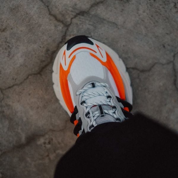 Top-down view of a white sneaker with orange accents on a cracked concrete surface.