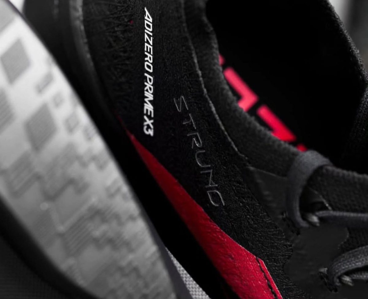 Close-up of a black running shoe with a red stripe and 'DIZERO PRIME X' branding along the side.