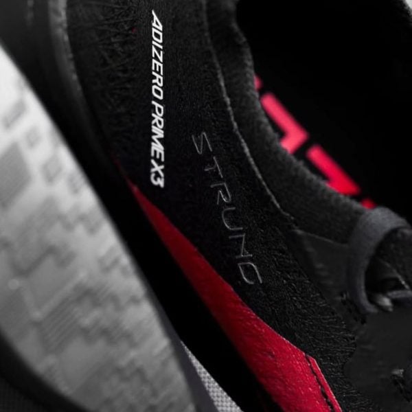Close-up of a black running shoe with a red stripe and 'DIZERO PRIME X' branding along the side.