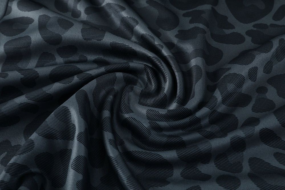 2eaaaf55 | UAE SPORT STORE Close-up of dark blue satin fabric with a subtle leopard print pattern twisted into a spiral.