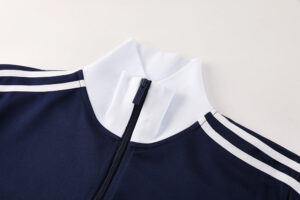 Close-up of a navy jacket with a white stand-up collar and a front zipper, featuring white stripes along the shoulders.