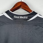 2f0fa79e_8c9f1cbf-db88-4d09-bb24-101dc6135d49 | UAE SPORT STORE Close-up of a Real Madrid jersey on a wooden hanger, focusing on the collar and club name "Real Madrid" embroidered on it.