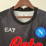 Close-up of a dark gray jacket on a wooden hanger, showing the neckline and a circular N logo patch on the right side of the image.