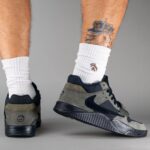 Gray and black sneakers on a person wearing white socks; tattooed calf visible in the background.