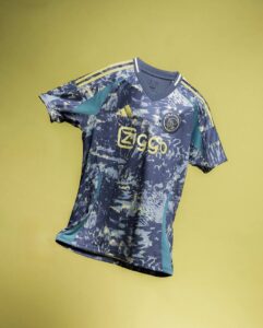 Ajax football jersey with blue camouflage pattern, yellow Ziggo logo, and Adidas stripes on shoulders against a yellow backdrop