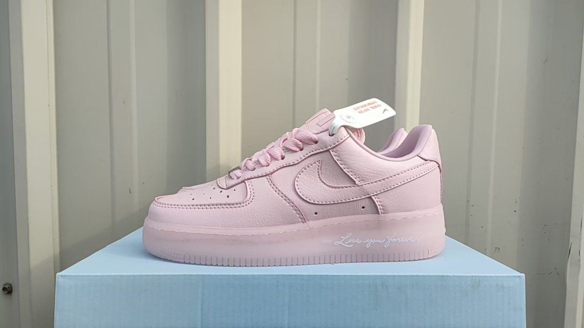 Pink Nike sneaker on a light blue box, side view showing the swoosh detail