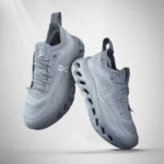 Two gray On running shoes shown midair, side and top views with breathable knit uppers and distinctive cloud sole pods.