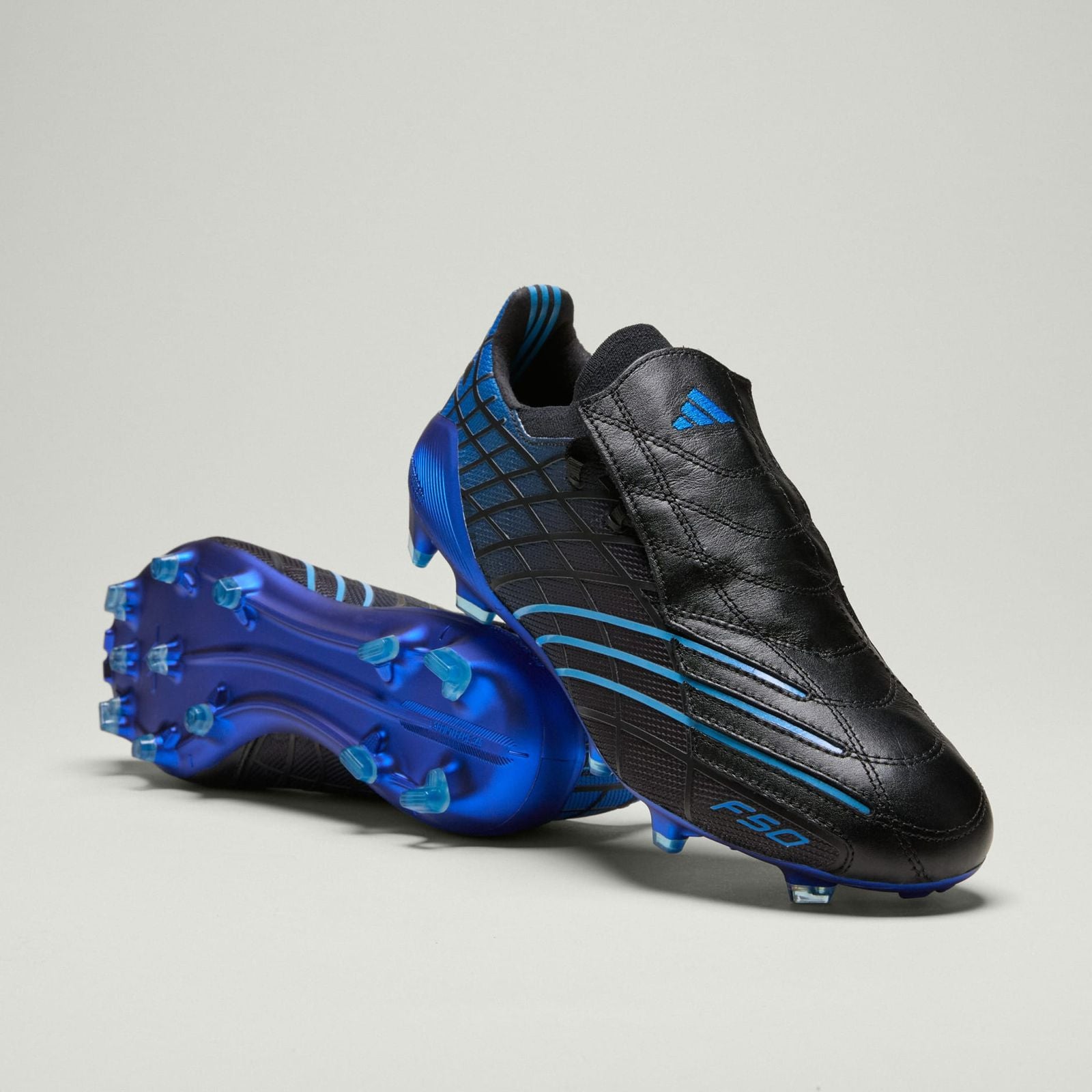 3088fd75-a1e8-42a7-8385-8235974698fb | UAE SPORT STORE Black and blue Adidas F50 soccer cleats with a blue studded sole set against a light gray background, angled to show the side and sole.