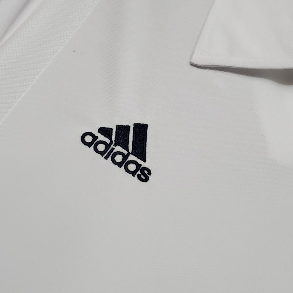 Close-up of white fabric with the Adidas logo partially visible in black letters, cropped at the bottom.